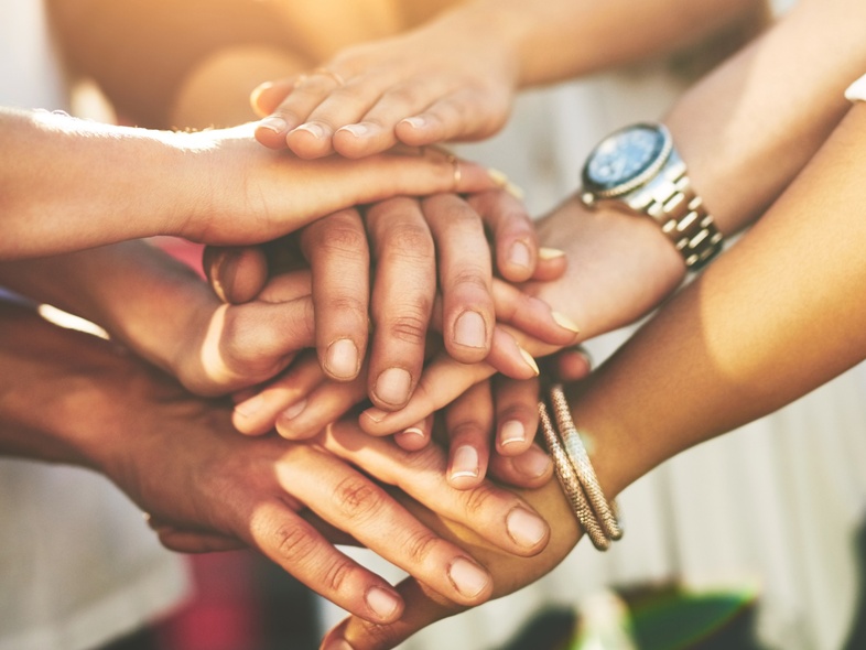 Flera personer lägger sina händer ovanpå varandra i en gemensam gest, närbild på händer