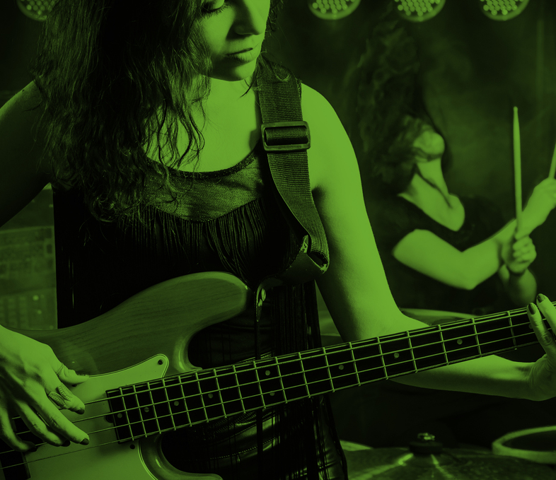 Två kvinnor spelar elbas och trummor på en scen, bilden har ett grönt filter.