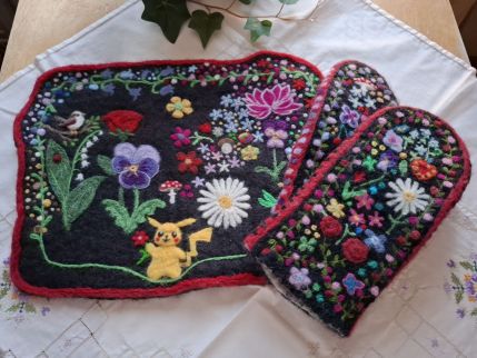 Broderad duk och vantar med färgglada blommor och Pikachu-motiv på en vit duk.