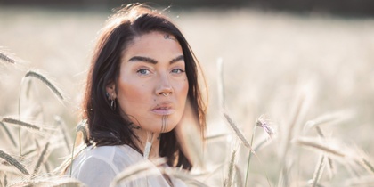 Person med långt hår står i ett fält av vete en solig dag. Ansiktet är suddat.