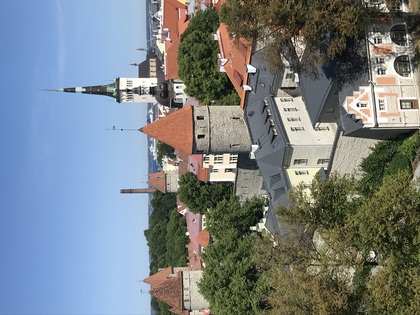 Utsikt över en gammal stad med torn, kyrka och röda tegeltak under en klarblå himmel.