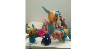 Flera färgglada, handgjorda gosedjur står på ett vitt bord i ett rum.