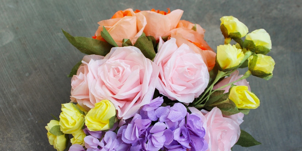 En bukett med färgglada konstgjorda blommor i rosa, lila, gult och orange på en grå bakgrund.