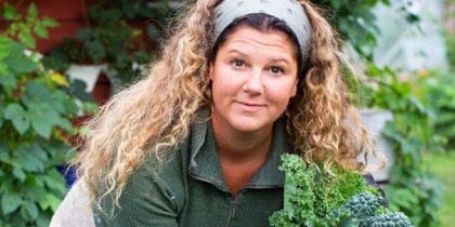 Kvinna med lockigt hår skördar grönkål i en grönskande trädgård.