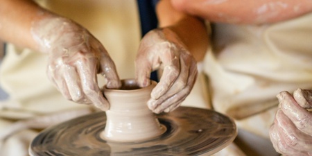 Två personer arbetar tillsammans med att forma lera på en drejskiva.