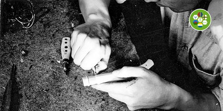 Svartvit bild. En person sitter och täljer. I högra hörnet syns en logotyp där symboler och flaggor för sveriges fem nationella minoriteter syns.