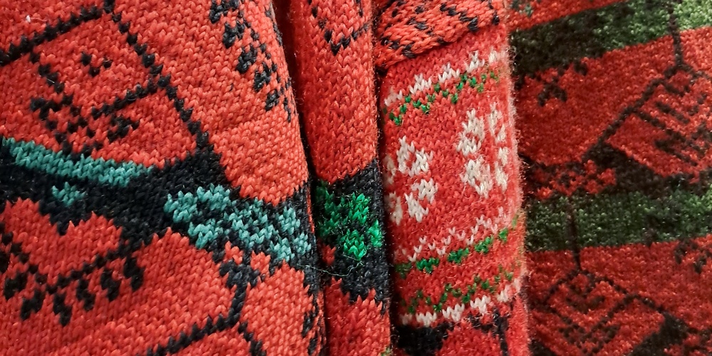 Närbild av röda stickade tröjor med traditionella delsbomönster i grönt, vitt och svart.