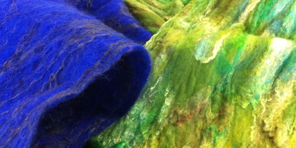 Närbild av blått och grönt tovade ulltyger med tydlig textur.