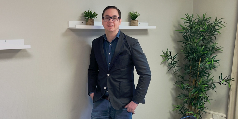 En person står vid väggen i ett mötesrum med bord, stolar, växter och hyllor med krukväxter.