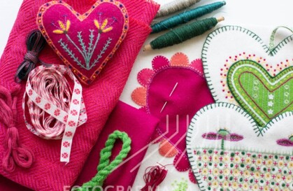 Färgglada broderade hjärtan, garn, band och tyg i rosa, grönt och vitt, arrangerade för handarbete.