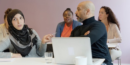 Fyra personer sitter vid ett bord i ett mötesrum och diskuterar, med en laptop och anteckningar framför sig.