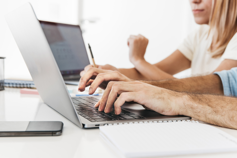 Två personer arbetar vid en bärbar dator med anteckningsblock och mobiltelefon på ett vitt skrivbord.
