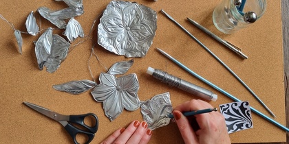En person arbetar med metallprägling och formar blommor och blad av tunn metall på en korkmatta.