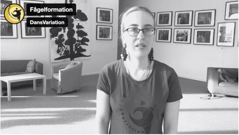 Person i t-shirt står i ett vardagsrum med soffor, bord och konst på väggarna.