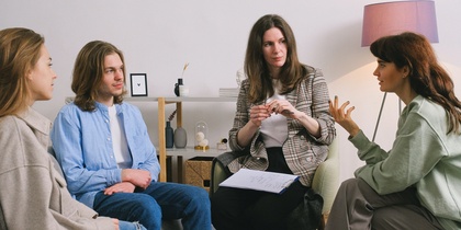 Fyra personer sitter i en cirkel och samtalar i ett ljust rum, en av dem antecknar på ett block.