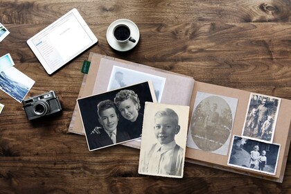Ett träbord med ett fotoalbum, gamla fotografier, en kamera, en kaffekopp och en surfplatta.