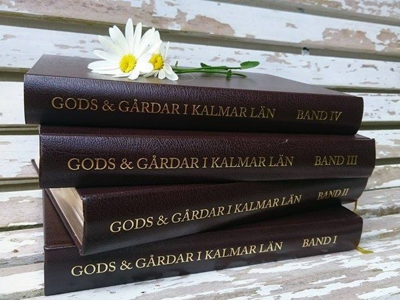 Fyra bruna böcker med titeln 'Gods & Gårdar i Kalmar län' ligger staplade på en sliten träbänk med två prästkragar ovanpå.