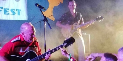 Livlig konsert med gitarrister på scen och entusiastisk publik nära scenen.