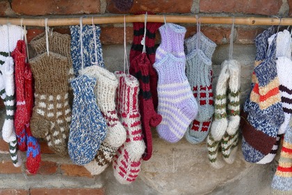 Flera par stickade sockor i olika färger hänger på en pinne mot en tegelvägg.