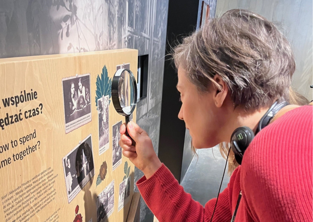 En person i röd tröja granskar en informationsskylt med förstoringsglas på ett museum.