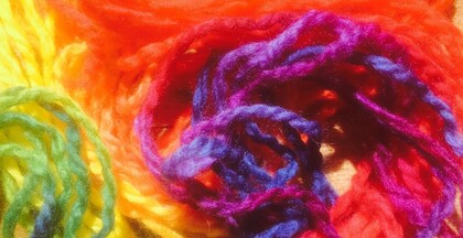Färgglada garntrådar i rött, gult, grönt, blått och lila ligger i en hög.