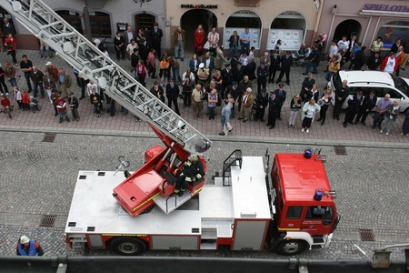 Brandbil med stege och brandmän på en gata, omgiven av en folksamling som tittar på.
