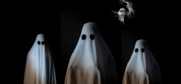 Tre personer utklädda till spöken med vita lakan och svarta ögon på en mörk bakgrund.