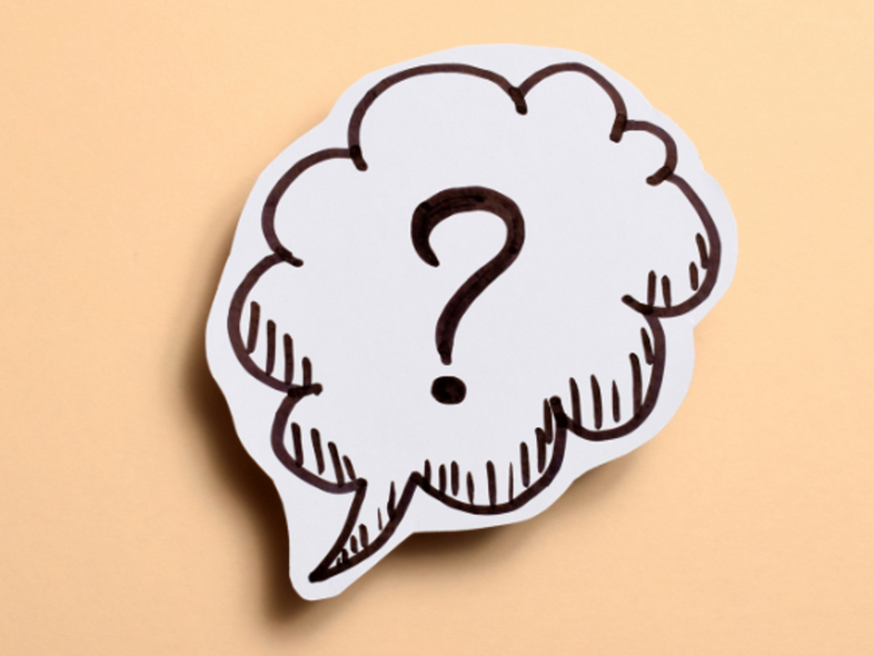 En pratbubbla med ett frågetecken ritad på vitt papper mot en beige bakgrund.