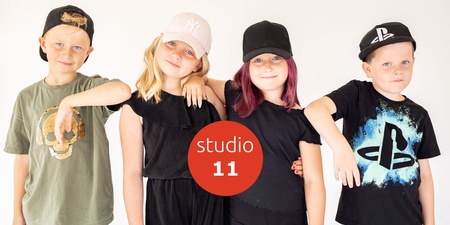 Fyra barn i kepsar poserar tillsammans framför en vit bakgrund med texten 'studio 11' i mitten.