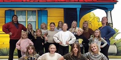 En grupp människor i olika åldrar står framför ett hus i glada färger.