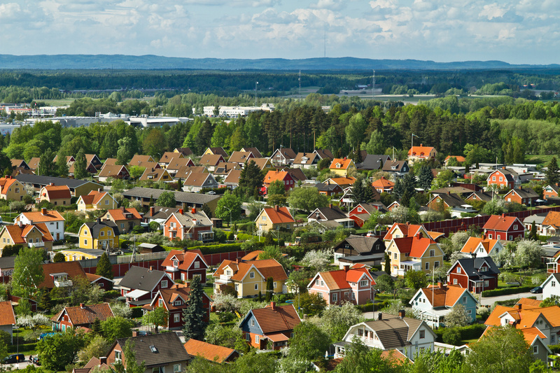 Färgglada villor med röda och gula tak i ett lummigt bostadsområde, omgivna av skog och berg i bakgrunden.