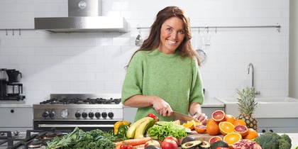 Person skär grönsaker och frukt i ett modernt kök med många färska råvaror på bänken.