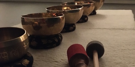 Fem tibetanska klangskålar står på rad på en matta med två klubbor framför dem i ett dämpat rum.