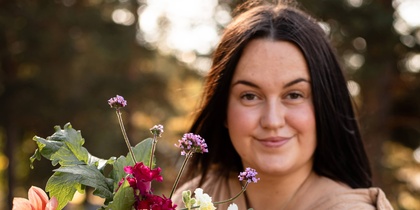 Person håller en stor bukett färgglada blommor utomhus i naturligt ljus.