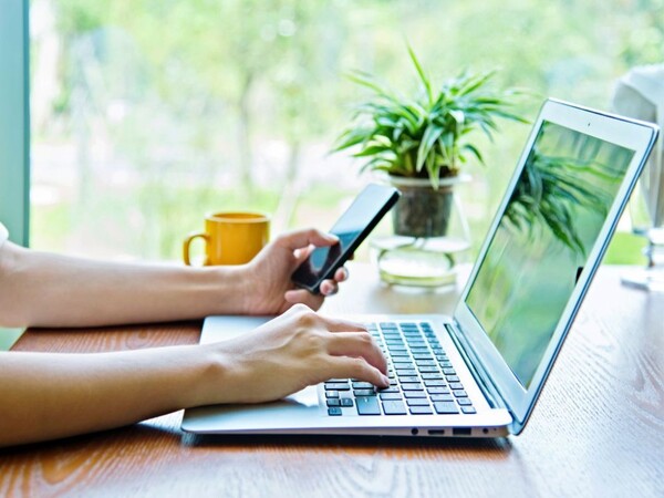 Två händer som arbetar på laptop och mobil.