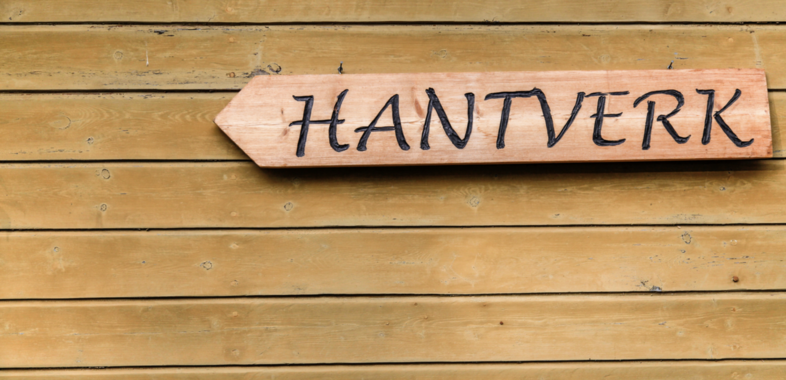 Träskylt med texten 'HANTVERK' på en gulbrun trävägg.