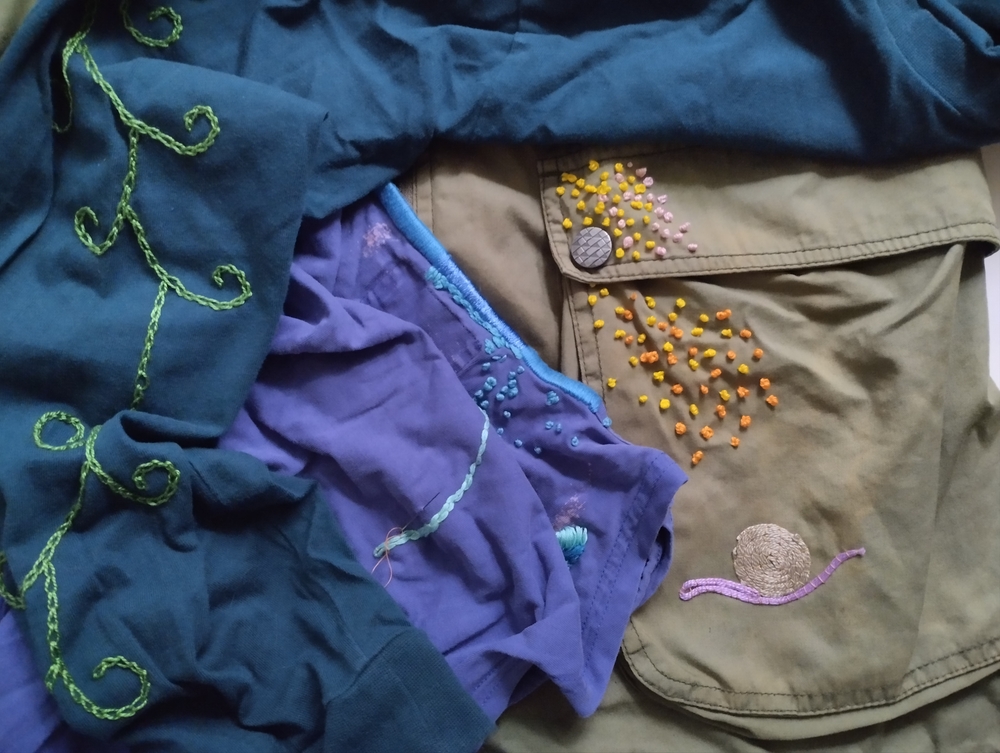 Färgglada kläder med broderade mönster och stygn i olika färger ligger i en hög.