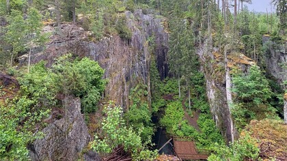 En djup ravin i en skog med branta klippor och tät grönska, samt en liten byggnad i botten.