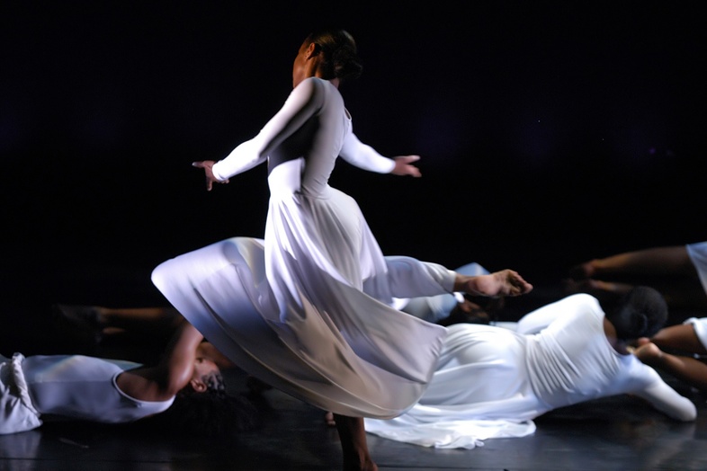 En dansare i vit klänning snurrar på scenen medan andra ligger på golvet i bakgrunden.