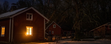 Röd stuga med tända fönster i snöigt landskap under stjärnklar natthimmel.