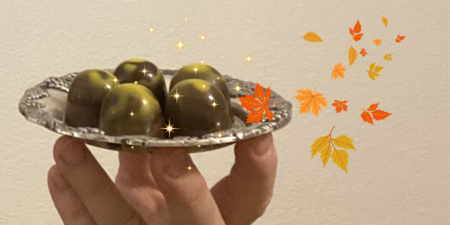 En hand håller ett silverfat med chokladpraliner, dekorerat med gnistrande effekter och höstlöv.