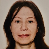 Porträttfoto av en person med axellångt mörkt hår och svart tröja mot ljus bakgrund.