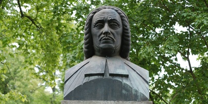 Byst av Olof Broman på en stenpelare i en grön park, med inskription på svenska.