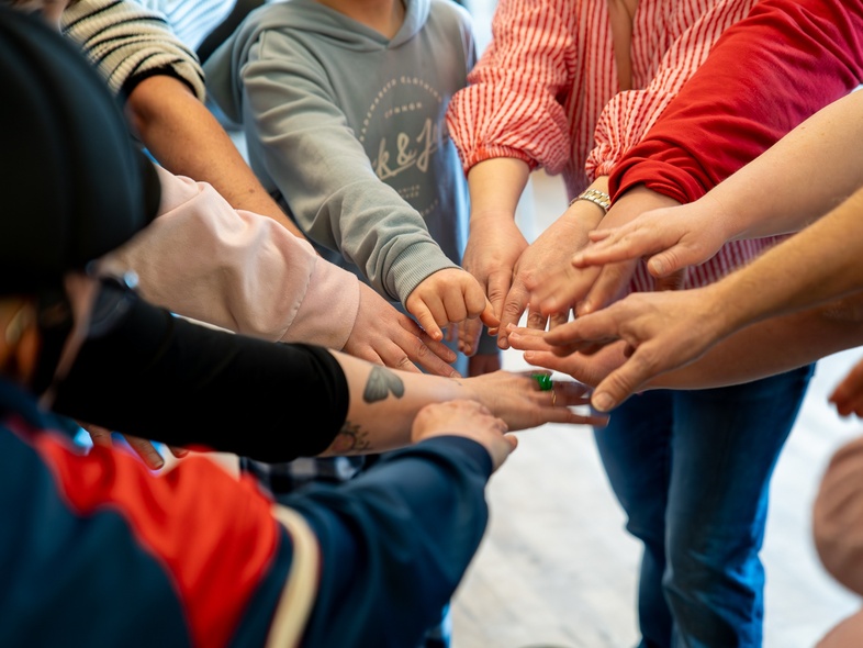 Flera personer står i en cirkel och sträcker in sina händer mot mitten för att röra vid varandra.