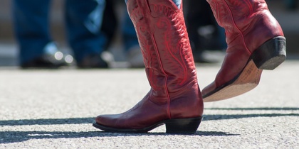 Person i blå jeans och röda cowboyboots dansar utomhus på asfalt.