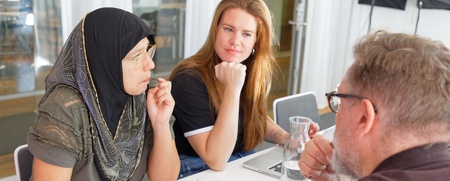 Tre personer sitter vid ett bord och diskuterar, med anteckningsblock och glas vatten framför sig.