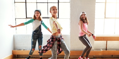 Tre unga personer dansar i ett ljust rum med stora fönster och trägolv.