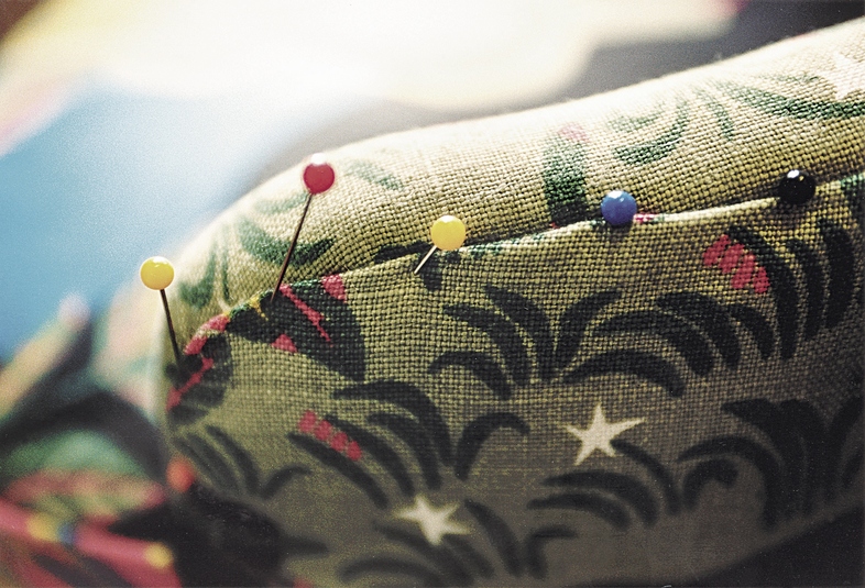 Flera knappnålar med färgade huvuden sitter fast i en tygbit med mönster.