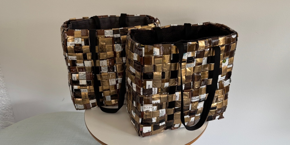 Två väskor flätade av återvunna kaffeförpackningar står på ett runt bord mot en vit vägg.