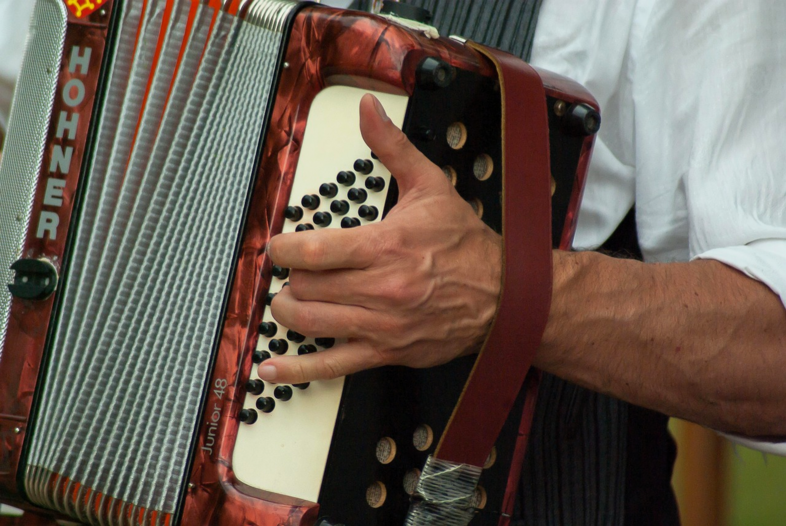 En person spelar på en röd dragspel av märket Hohner, fokus på handen och instrumentet.